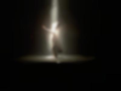 A person wearing a tall hat and a cape is at the center of the stage, with one of their arms raised. A spotlight shines on top of them.