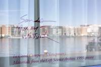 A reflection on a glass surface shows a river and buildings on the opposite bank. In purple text, the following text appears: 