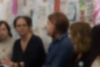 Five people sit in line. Behind them, there is a wall with drawings and hand-drawn posters.