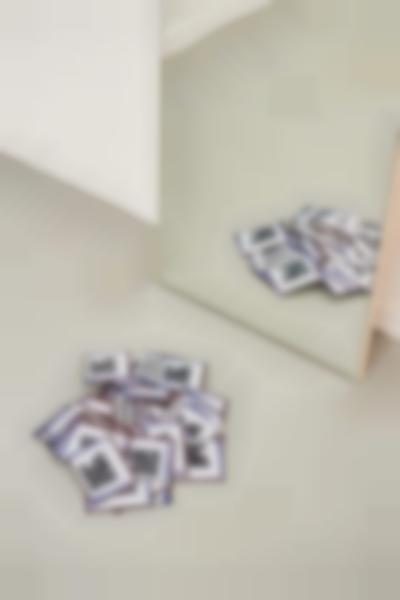 On the floor, several copies of the same image are piled up. A mirror is propped against the wall, showing the reflection of the stack of images.