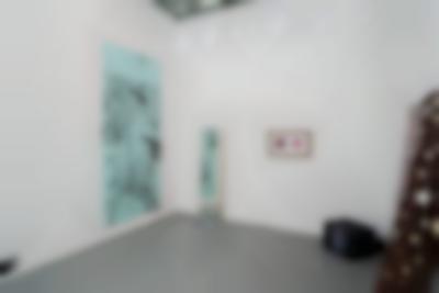 Indoor space with white walls and grey floor. Around the room, there is a large blue screen, a mirror, a frame, a TV set and a mixed media installation. These are all hanging or propped against the walls, except for the TV which is on the floor, in the right corner. On the large blue screen there is a hand-drawn horse with rounded black text at the top, reading: 