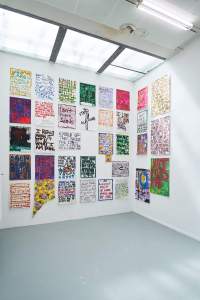 Indoor space with white walls and grey floor. The visible wall space is filled with hand-drawn posters, hanging from floor to ceiling.