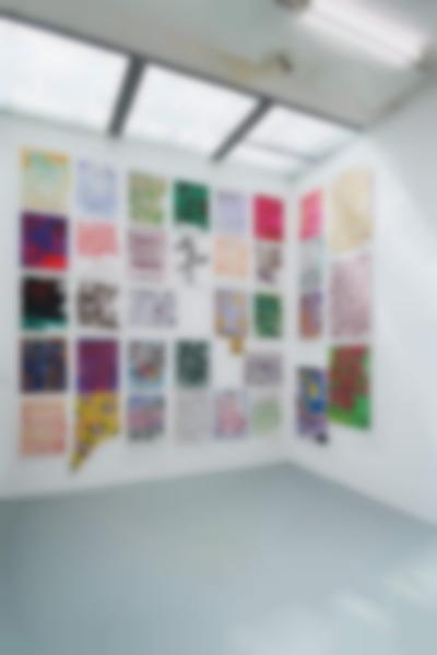 Indoor space with white walls and grey floor. The visible wall space is filled with hand-drawn posters, hanging from floor to ceiling.