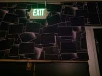 Black wall with a black wallpaper with white shapes. On the wall, there is a lit up, green 