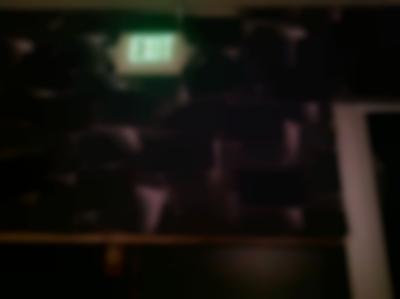 Black wall with a black wallpaper with white shapes. On the wall, there is a lit up, green 