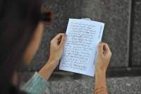 Two hands hold a paper with handwritten notes. The person's head is out of focus, but partially visible on the left side of the photograph.