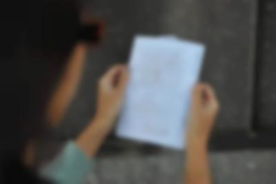 Two hands hold a paper with handwritten notes. The person's head is out of focus, but partially visible on the left side of the photograph.