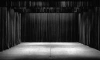 Empty stage with black curtains. There is a microphone stand in the middle, at the front.