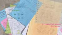 Several colourful sheets of paper with handwritten notes have been loosely stacked. A digital page with text and images has been superimposed on the image. On the bottom right, 