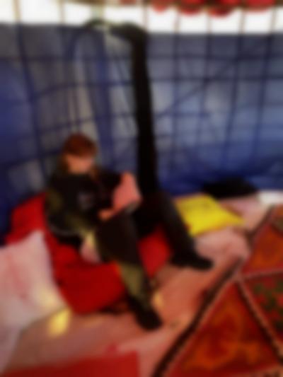 A person is sitting on a red bean bag next to a structure that is closed off with a purple textile. The person is leafing through a book. There are two other pillows, one of which says 