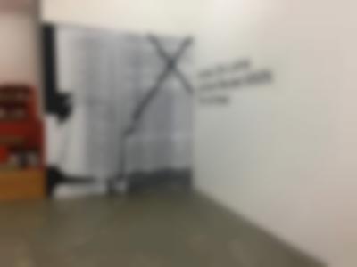 Curtain printed with a montage of several word documents. There is a large cross on top of the image occupying the right half of the curtain. On the wall, next to it, a black text reads: 