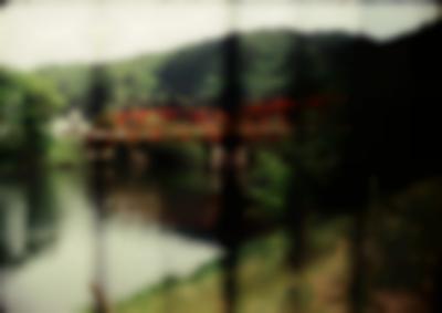 River with red bridge. There is green vegetation on the river banks. Several bars are out of focus, in the forefront of the photograph.