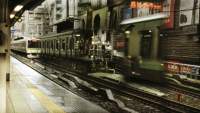 A moving train is arriving to the platform. There is some reflections in the image, perhaps from double exposure.
