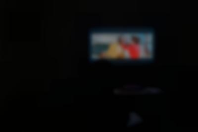 Dark space. Only the projection of a film is visible.  The image shows a feminine-presenting person touching the head of another person.