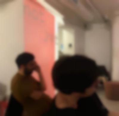 Two people sit facing the same direction. Behind them, there is wall projection of a red block with the words 