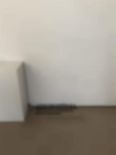 A wall text appears at the bottom of a wall; the first line appears on the wall, with the remaining of the text on the beige floor. To the left, a white plinth remains empty. The text reads 