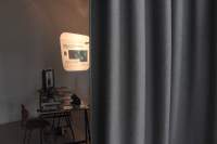 A grey curtain occupies two thirds of the image. To the left, a table with books and other printed materials is visible. An image and some text is being projected on the wall next to it.