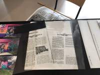 On a table with black cloth, two transparency sheets with black text have been left on top of a white booklet. The title of the right transparency sheet is 