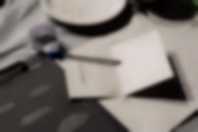 Table with three different printed materials, a pen, a white paper strip with zigzag edges and the edge of a plate. The printed materials are either white or black, and have text printed on.