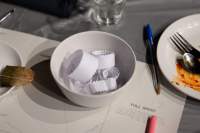 A small white porcelain bowl has several white paper strips with zig zag edges in it. Around it, there is a paper with 